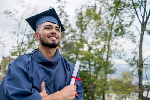 Graduação: homem jovem trajando beca de formatura com seu diploma em mãos